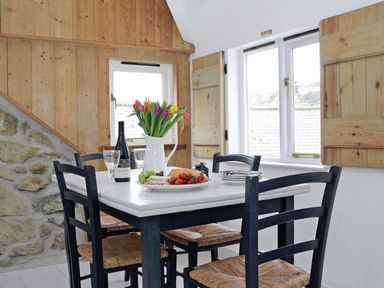 A dining area with a white table black chairs a plate of food a bottle of wine glasses and flowers at The Net Loft in Mousehole