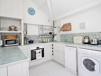 A kitchen with white cabinets a microwave oven dishwasher washing machine kettle and toaster at The Net Loft in Mousehole
