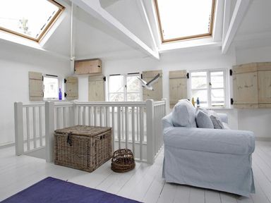 A bright room with skylights white railing wicker baskets and a light blue sofa with cushions at The Net Loft in Mousehole