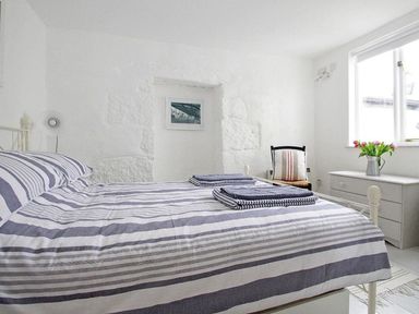 A bedroom with a bed covered in striped bedding two folded towels a chair a chest of drawers with flowers and a window at The Net Loft in Mousehole