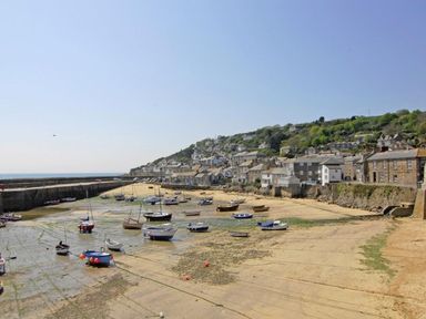A harbor with boats on sand and water near a village with hillside houses at The Net Loft in Mousehole