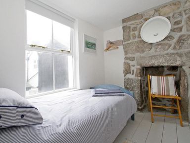 A bedroom with a single bed near a window stone wall with a chair and a round mirror at The Net Loft in Mousehole