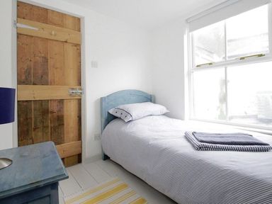 A small bedroom with a single bed next to a window and a wooden door at The Net Loft in Mousehole