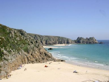 A sandy beach with people on the shore and rocky cliffs along the coastline at The Net Loft in Mousehole