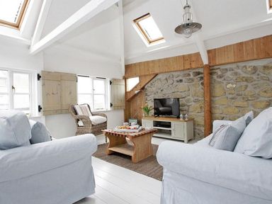 A living room with two white sofas a wooden coffee table a wicker chair a TV on a cabinet and skylights at The Net Loft in Mousehole