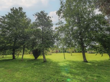 A grassy park-like area with scattered medium-sized trees under a partly cloudy sky at The Stables in Ruthvoes near St Columb Major