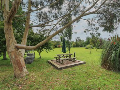 A garden with trees a wooden picnic table with an umbrella and a hanging chair from a tree at The Stables in Ruthvoes near St Columb Major