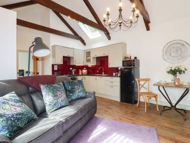 An open plan living room and kitchen with a gray sofa and floral cushions at The Stables Ruthvoes near St Columb Major