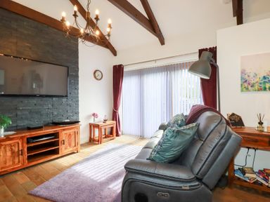 A living room with a gray leather sofa pillows and lamp next to a wooden TV cabinet and stone wall at The Stables in Ruthvoes near St Columb Major