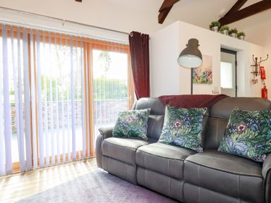 A living room with a black sofa with patterned cushions and a floor lamp near sliding glass doors at The Stables in Ruthvoes near St Columb Major