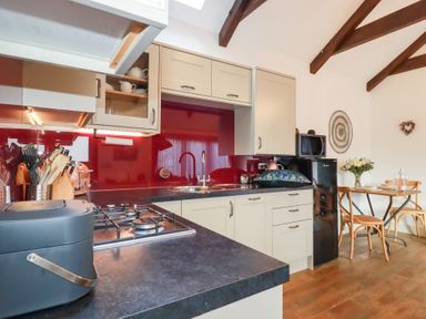 A kitchen with white cabinets black countertop red backsplash and a dining table with chairs at The Stables in Ruthvoes near St Columb Major