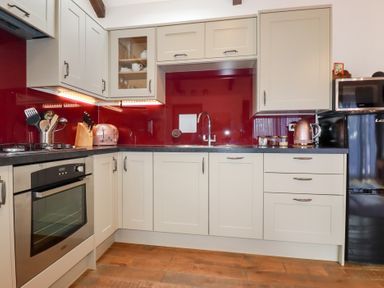 A kitchen with beige cabinets a red backsplash stainless steel oven toaster and kettle at The Stables in Ruthvoes near St Columb Major