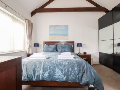 A bedroom with a double bed two bedside tables and lamps a large wardrobe and a window at The Stables Ruthvoes near St Columb Major