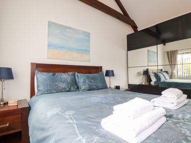 A bedroom with a bed with folded towels on it two bedside tables with lamps a painting on the wall and mirrored wardrobes at The Stables in Ruthvoes near St Columb Major