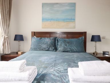 A bedroom with a bed covered in blue bedding and folded white towels on the foot of the bed two bedside tables with lamps and a painting above the bed at The Stables in Ruthvoes near St Columb Major