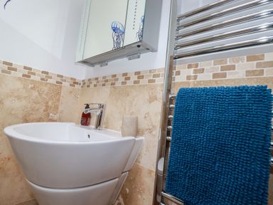 A bathroom sink with a soap dispenser and cup and a blue towel on a metal towel rack