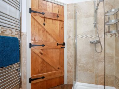 A shower area with a wooden door and a towel on a heated rack in a bathroom at The Stables in Ruthvoes near St Columb Major