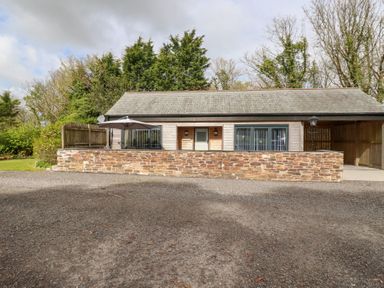 A single-story house with a stone wall and an umbrella in front at The Stables in Ruthvoes near St Columb Major