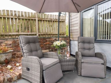 An outdoor seating area with two grey cushioned chairs a glass table with flowers and a bottle under a large umbrella at The Stables in Ruthvoes near St Columb Major