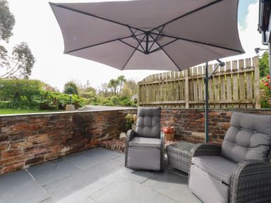 An outdoor patio with two cushioned chairs a small table and a large umbrella at The Stables Ruthvoes near St Columb Major
