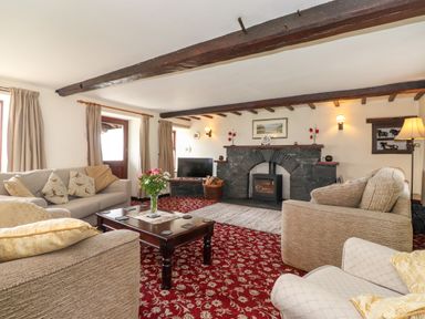 A living room with sofas a wooden coffee table a stone fireplace and a television at Addyfield Farmhouse in Cartmel Fell near Bowland Bridge