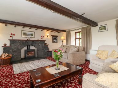 A living room with a stone fireplace wooden beams and sofas at Addyfield Farmhouse Cartmel Fell near Bowland Bridge