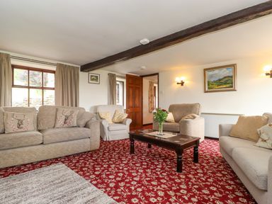 A sitting room with sofas and armchairs around a wooden coffee table on a patterned red carpet at Addyfield Farmhouse in Cartmel Fell near Bowland Bridge