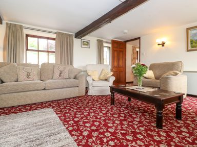 A living room with two sofas an armchair wooden coffee table and floral carpet at Addyfield Farmhouse in Cartmel Fell near Bowland Bridge