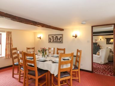 A dining room with a wooden table set with plates glasses and flowers at Addyfield Farmhouse Cartmel Fell near Bowland Bridge