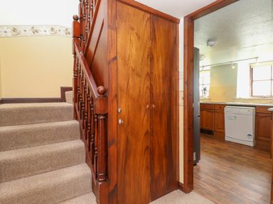 A staircase with wooden banister and a wooden cupboard door under the stairs leading to a kitchen with wooden cabinets and a dishwasher at Addyfield Farmhouse Cartmel Fell near Bowland Bridge