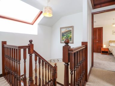 A stairway with wooden banisters next to a bedroom with a bed a nightstand and a closet at Addyfield Farmhouse in Cartmel Fell near Bowland Bridge