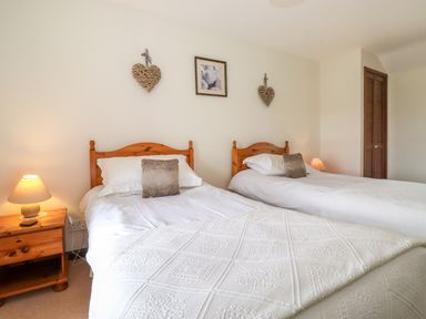 A bedroom with two single beds wooden headboards bedside tables with lamps and wall decorations at Addyfield Farmhouse in Cartmel Fell near Bowland Bridge