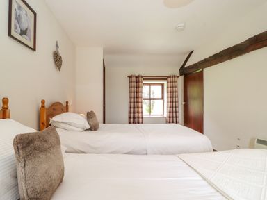 A bedroom with two single beds white bedding wooden headboards and window with plaid curtains at Addyfield Farmhouse Cartmel Fell near Bowland Bridge