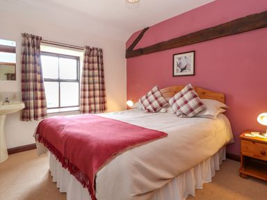 A bedroom with a double bed featuring plaid pillows and a red throw blanket near a window with plaid curtains at Addyfield Farmhouse in Cartmel Fell near Bowland Bridge