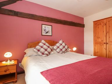 A bedroom with a double bed plaid pillows and wooden furniture at Addyfield Farmhouse Cartmel Fell near Bowland Bridge