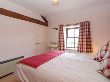 A bedroom with a double bed with red and white plaid pillows and curtains and a small sink under a window at Addyfield Farmhouse Cartmel Fell near Bowland Bridge