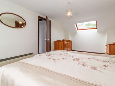 A bedroom with a bed, wooden crib, wooden dresser, oval mirror on the wall, and skylight window at Addyfield Farmhouse in Cartmel Fell near Bowland Bridge