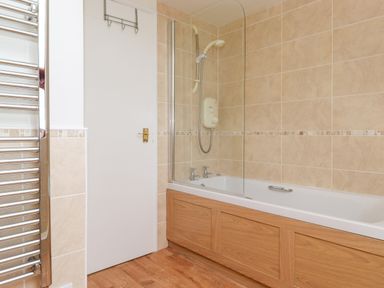 A bathroom with a bathtub that has a shower and glass screen and a white door with a towel rail at Addyfield Farmhouse Cartmel Fell near Bowland Bridge