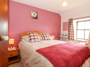 A bedroom with a double bed with plaid pillows bedside tables lamps a window and a sink at Addyfield Farmhouse in Cartmel Fell near Bowland Bridge
