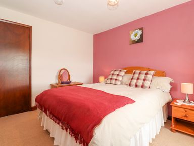 A bedroom with a bed with checked pillows and red throw blanket and bedside tables with lamps at Addyfield Farmhouse in Cartmel Fell near Bowland Bridge