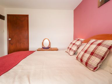 A bedroom with a bed with checkered pillows and a wooden headboard a wooden door and a small wooden table with a mirror at Addyfield Farmhouse Cartmel Fell near Bowland Bridge
