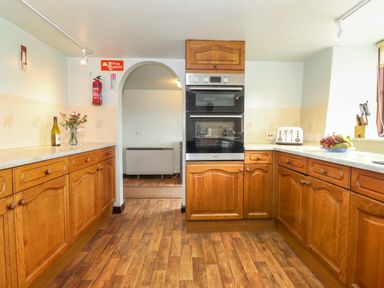 A kitchen with wooden cabinets a built-in oven a toaster a fruit bowl and a bottle of wine at Addyfield Farmhouse in Cartmel Fell near Bowland Bridge