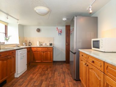 A kitchen with wooden cabinets a dishwasher a microwave a refrigerator and a clock on the wall at Addyfield Farmhouse in Cartmel Fell near Bowland Bridge
