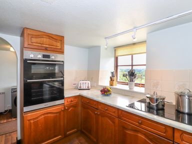 A kitchen corner with wooden cabinets a double oven a toaster pots utensils and a window at Addyfield Farmhouse in Cartmel Fell near Bowland Bridge