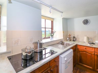 A kitchen with pots on a stove a sink a dishwasher a window and wooden cabinets at Addyfield Farmhouse Cartmel Fell near Bowland Bridge
