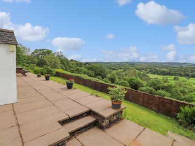 An outdoor patio area with potted plants overlooking a green landscape and wooden fence at Addyfield Farmhouse in Cartmel Fell near Bowland Bridge