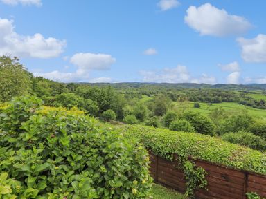 A landscape view of green fields trees and hills under a blue sky with clouds at Addyfield Farmhouse in Cartmel Fell near Bowland Bridge