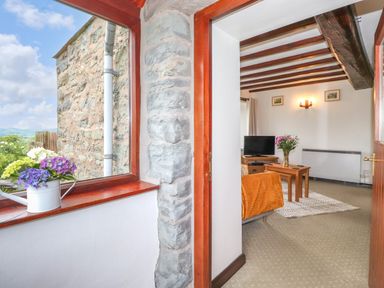 A living room with a television flowers on a table and wooden beams on the ceiling at Addylea Cottage in Cartmel Fell near Windermere