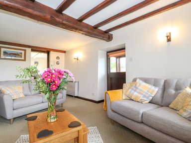A living room with two gray sofas a wooden coffee table with flowers and exposed wooden beams on the ceiling at Addylea Cottage in Cartmel Fell near Windermere