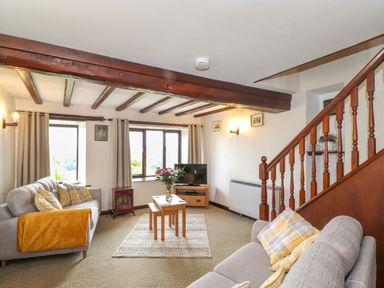 A living room with two sofas wooden beams wooden staircase and a television at Addylea Cottage in Cartmel Fell near Windermere